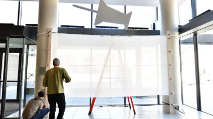 Two people installing a large white screen in a modern building lobby