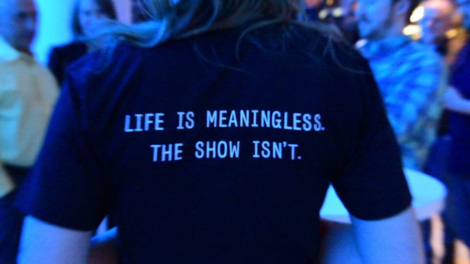 Person wears black T-shirt with blue text: "Life is meaningless. The show isn't."