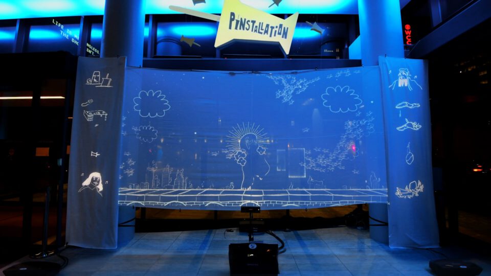 Interactive blue projection wall with white sketches and "PinInstallation" sign