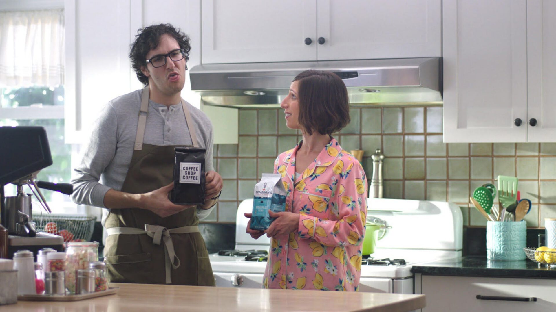 Man and woman in kitchen holding coffee products, smiling at each other.