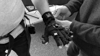 Person wearing sensor glove being adjusted by another person
