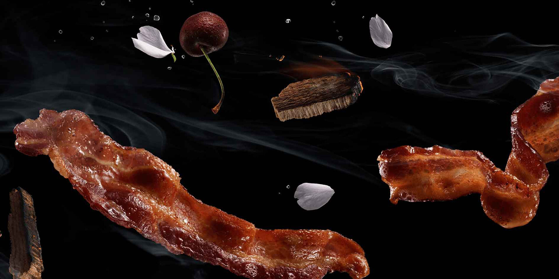 Crispy bacon strips floating with smoke, cherry, and petals against black background