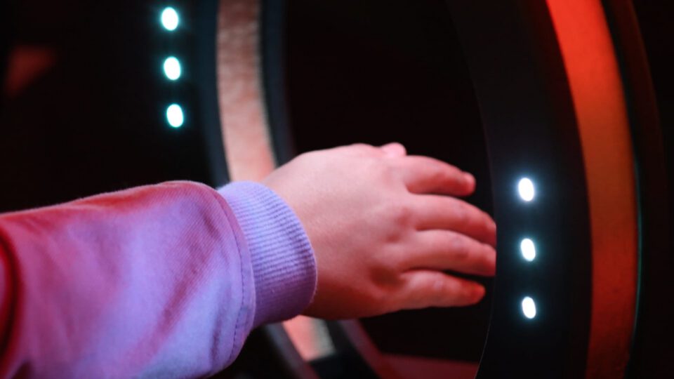 Child's hand touching illuminated interactive display with glowing dots