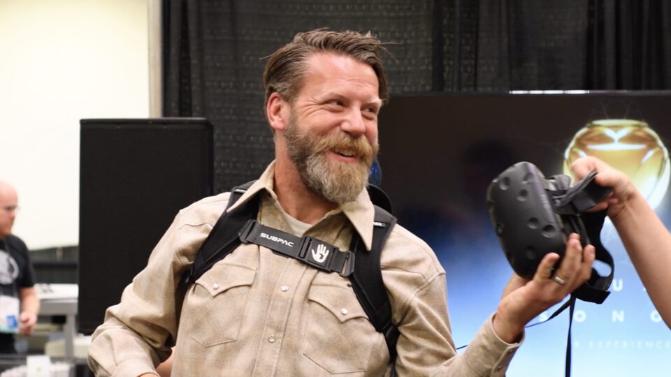 Man with beard smiles while wearing VR headset harness.
