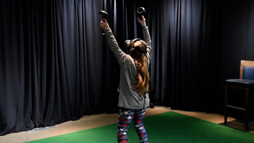 Child immersed in VR, arms raised, wearing headset and controllers.