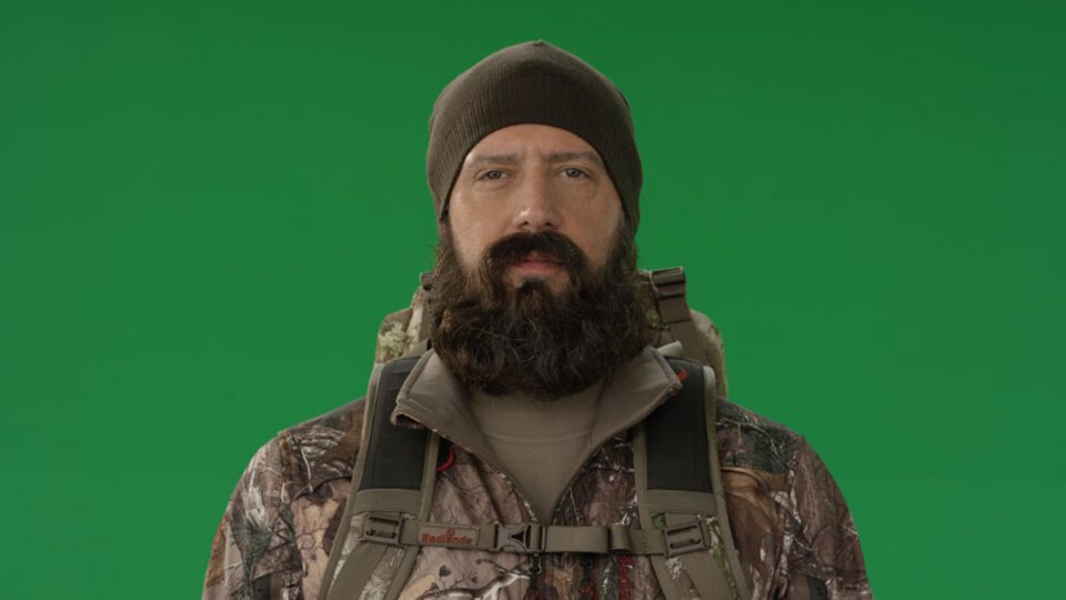 Man with beard and beanie in camouflage gear against green screen