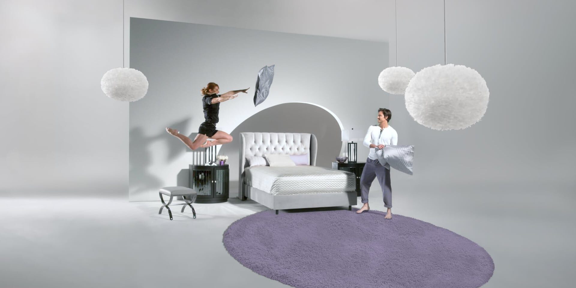 Two people playfully tossing pillows in a modern bedroom with floating lights.