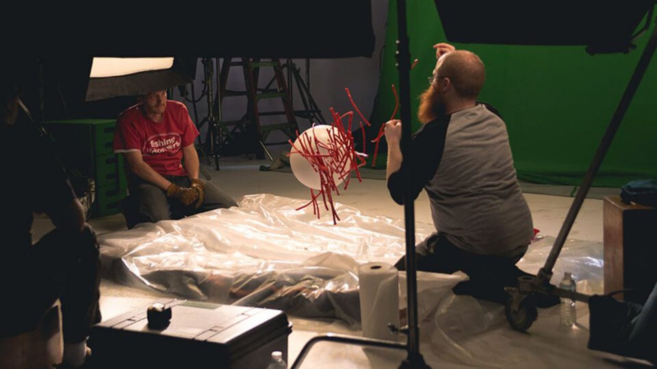 Studio crew works on red wire sculpture with green screen backdrop