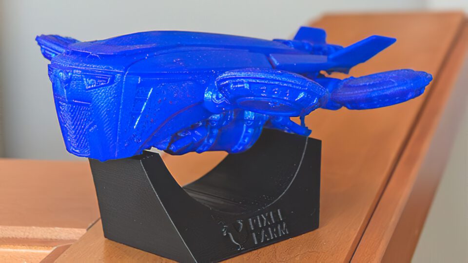 Blue 3D-printed spaceship model on black display stand labeled "PIXII FARM"
