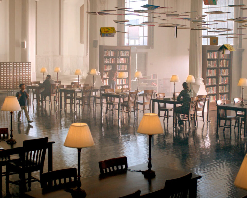 Grand library with high ceilings, bookshelves, tables, lamps, and people reading.