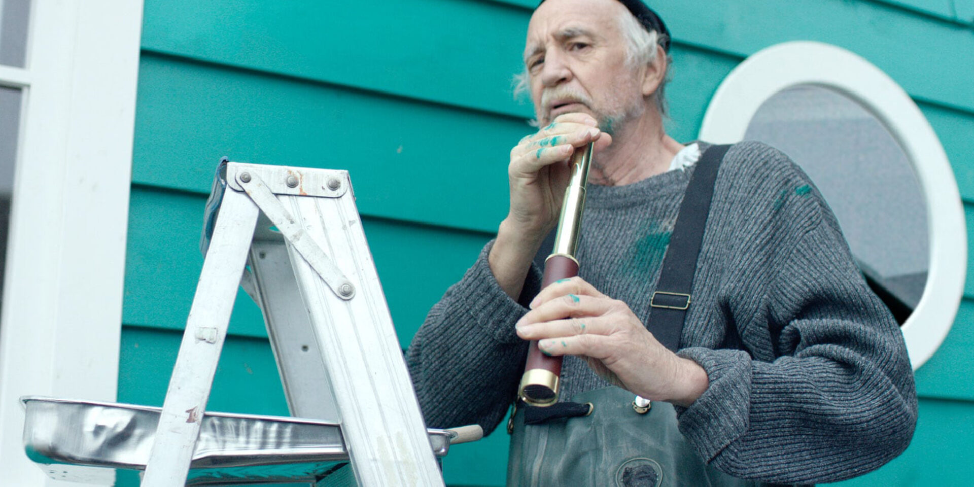 Elderly man paints house while holding a telescope-like object