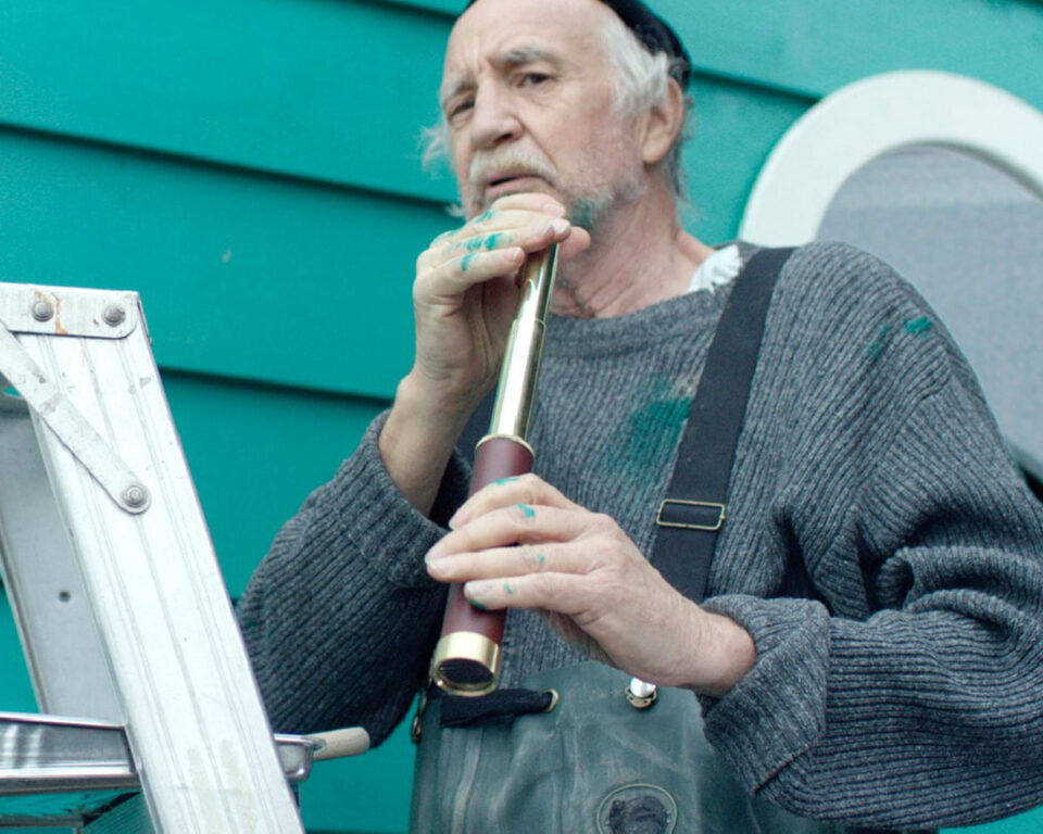 Elderly painter with a telescope wearing overalls and paint-splattered clothes.