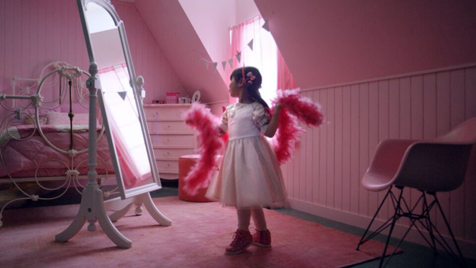 Little girl in pink room holding feather boas, standing before mirror