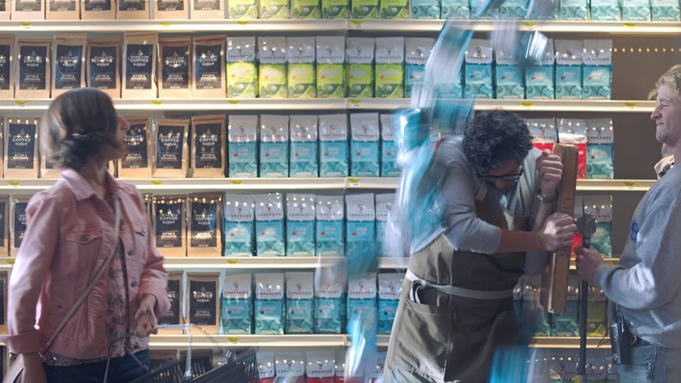 Three people interact near coffee shelves, one with motion blur.
