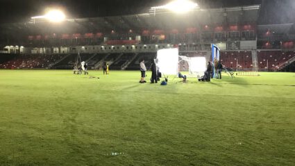 Film crew sets up lights on empty stadium field at night