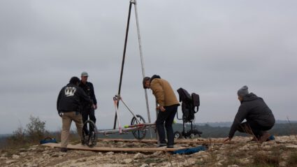 Four people assemble a portable ramp on uneven terrain near a mobility scooter.