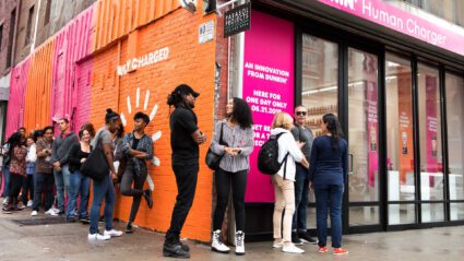 People queue outside Dunkin' Human Charger pop-up, vibrant pink and orange storefront