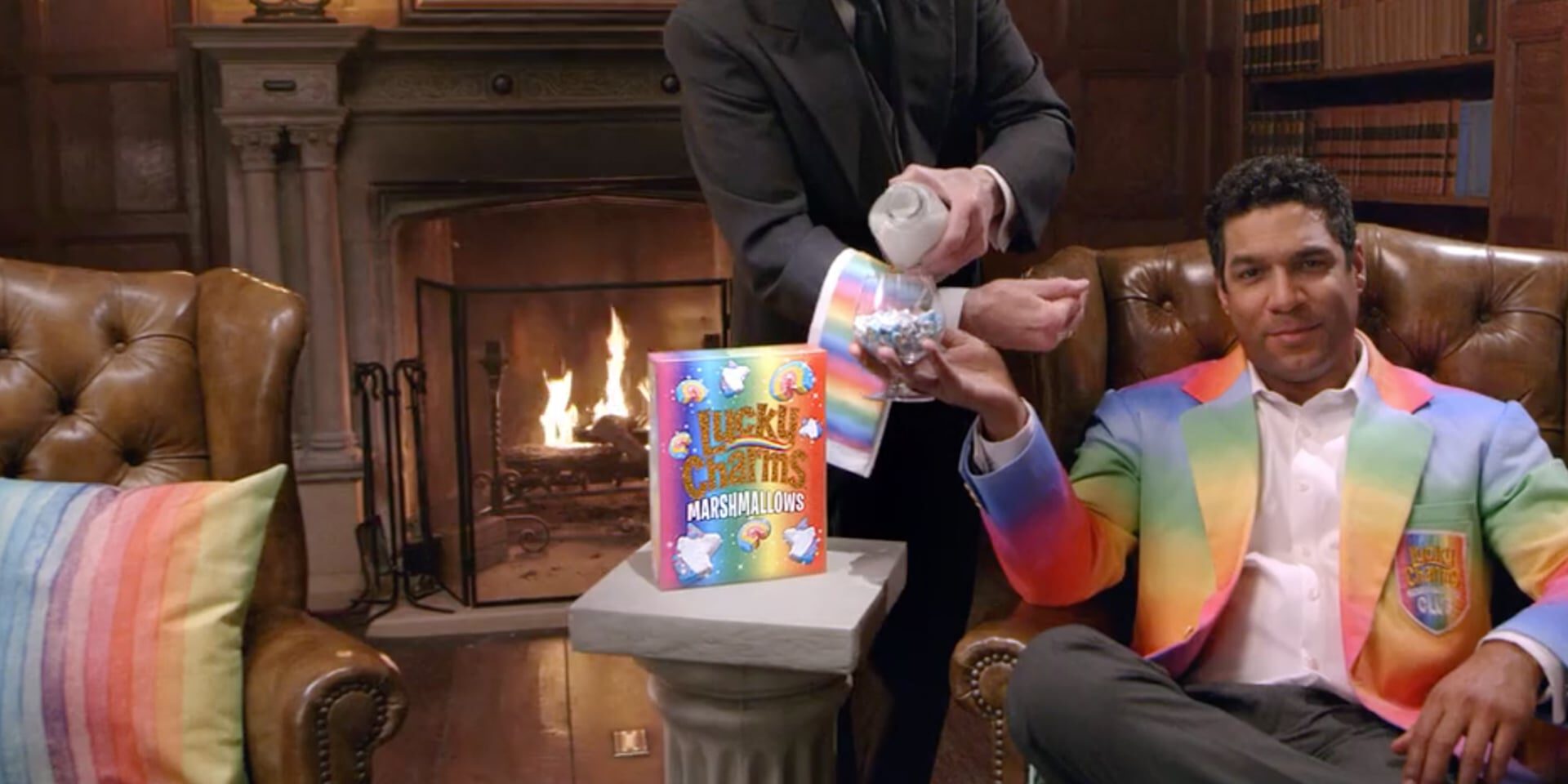 Man in rainbow suit receives Lucky Charms marshmallows from server by fireplace