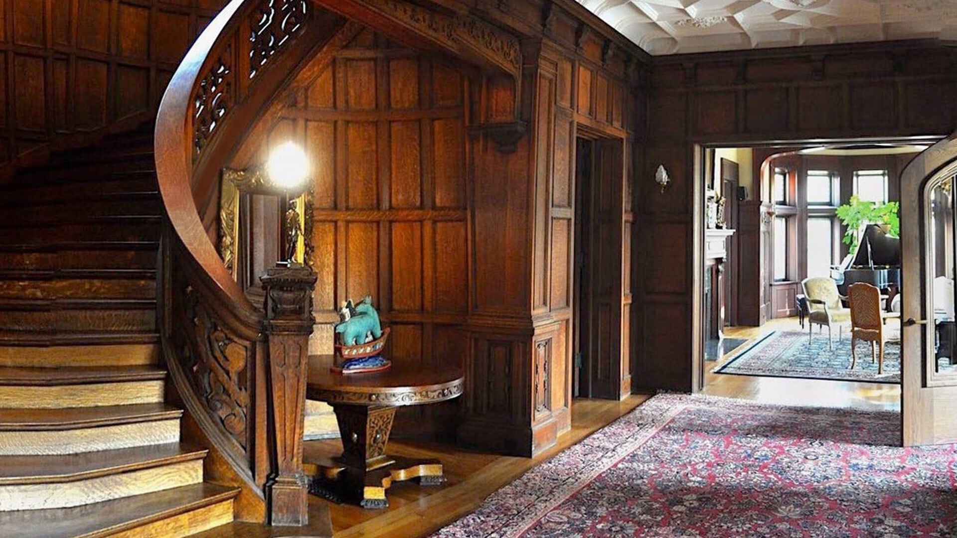 Grand wooden staircase with ornate railing in a historic home foyer.