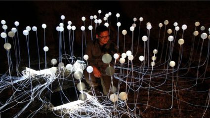 Person surrounded by glowing orbs on wires in dark outdoor setting