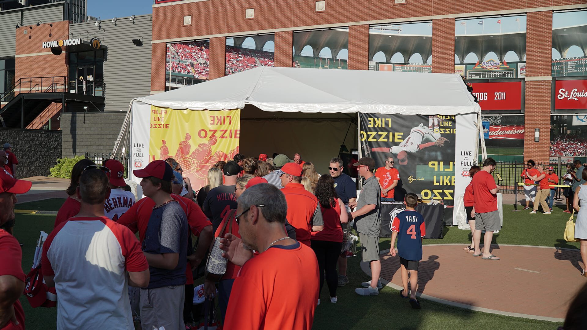 Fans in red gather near a tent at a baseball stadium event.
