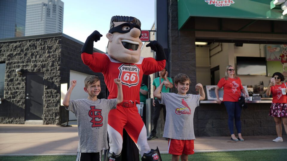 Two boys pose with a Phillips 66 mascot at a Cardinals event.