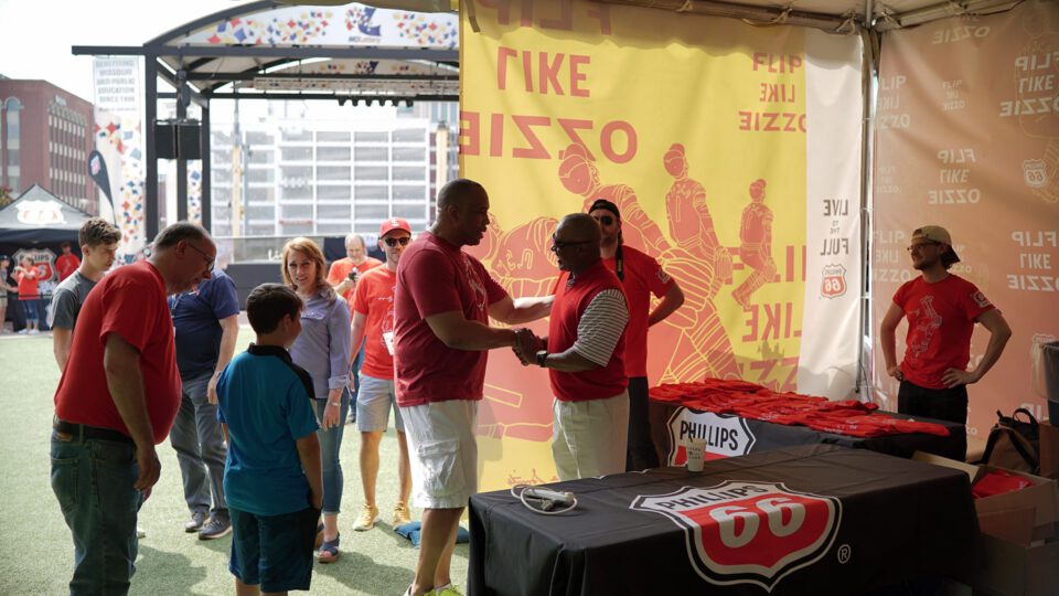 Baseball event with fans, players, and branded merchandise under a tent.