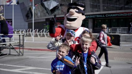 Children posing with a mascot outside a basketball arena