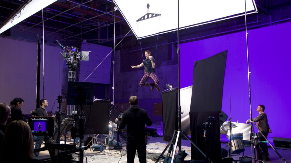 Actor suspended by wires in studio, crew operating cameras and lights