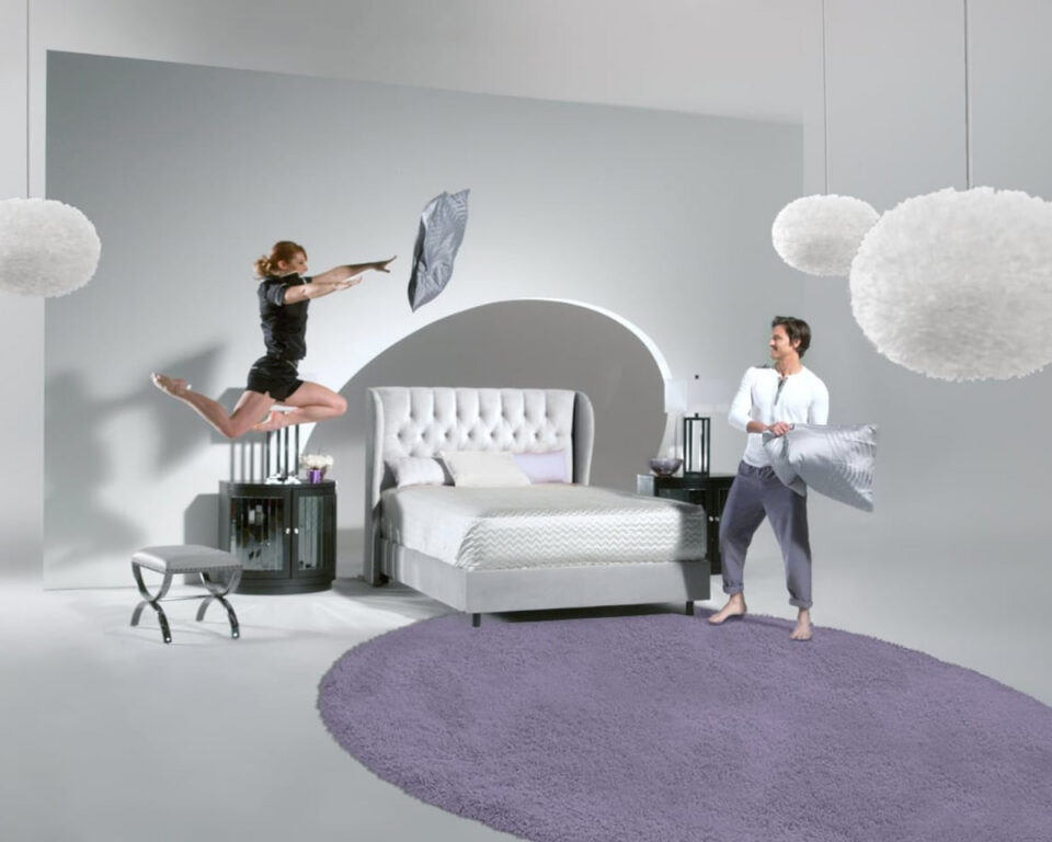 Two people playfully tossing pillows in a modern bedroom with purple rug.