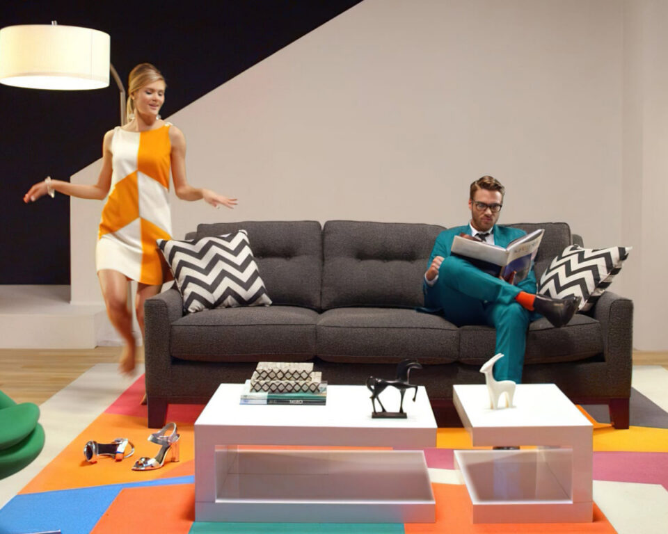 Woman in geometric dress walks past man reading on modern sofa.