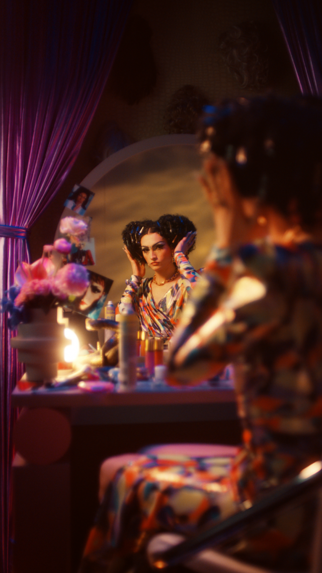 Drag queen in colorful dress admiring reflection in vanity mirror with purple curtains