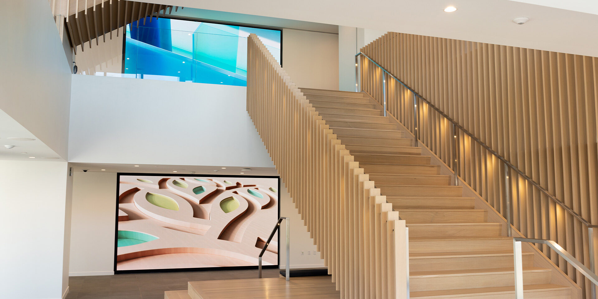 Modern wooden staircase with handrails, abstract art, and blue glass railing above.