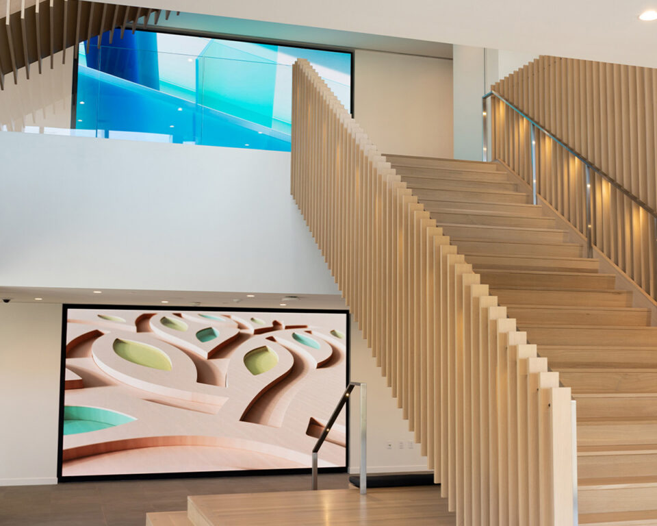 Modern wooden staircase with glass railing, abstract art walls, and bright interior lighting.