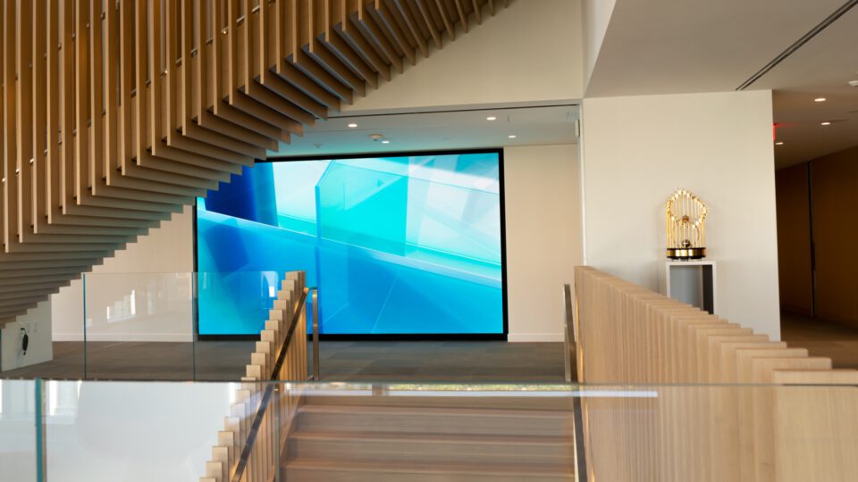 Modern atrium with wooden staircase, glass rail, and large blue screen display.