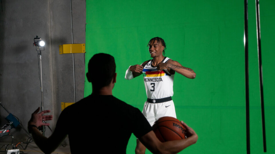 Basketball player in Minnesota jersey poses in front of green screen with photographer.