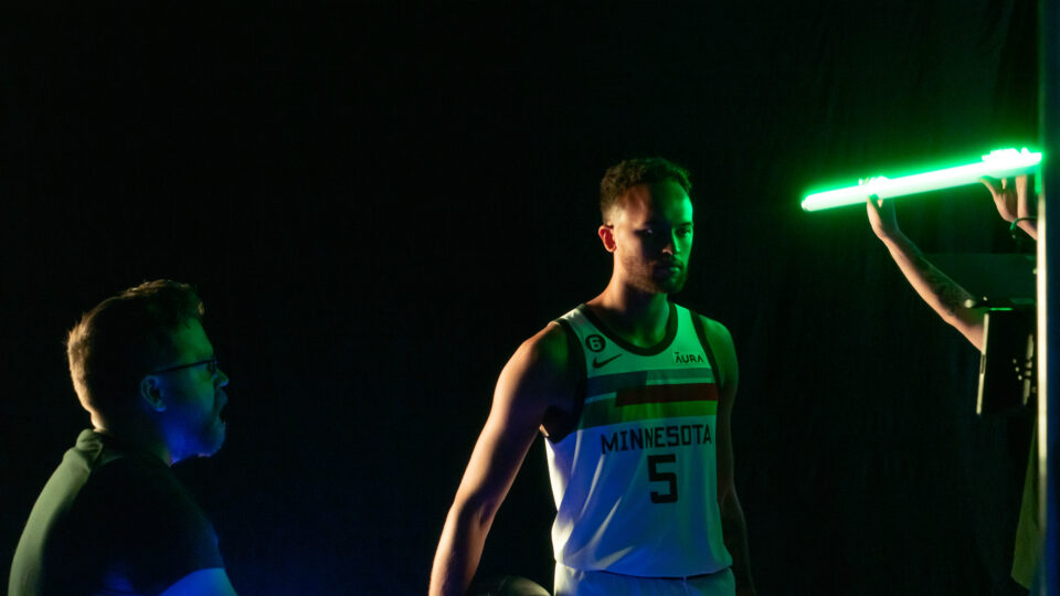 Basketball player in Minnesota jersey holding ball under neon lights