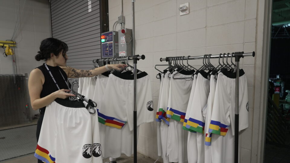 Woman organizing white jerseys with rainbow trim on racks in a warehouse.