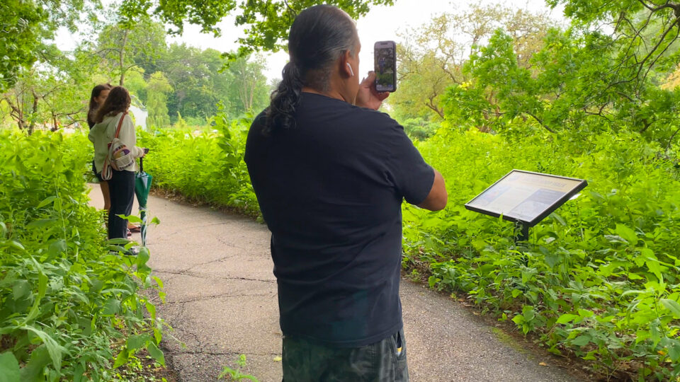 Man with long hair taking photo of nature trail sign