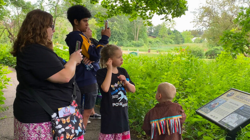 Family exploring outdoor garden with informational sign and lush greenery