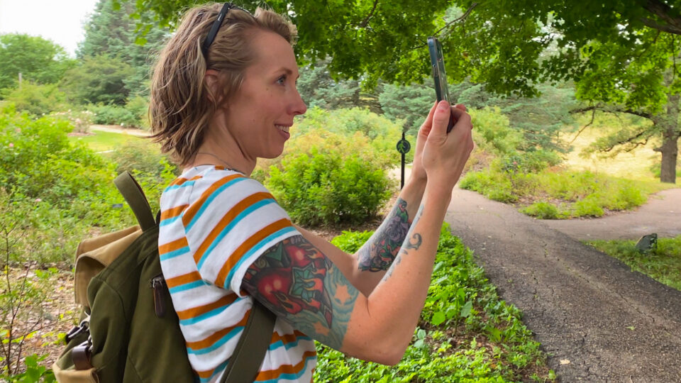 Woman with tattoos uses Revelo App outdoors in garden setting