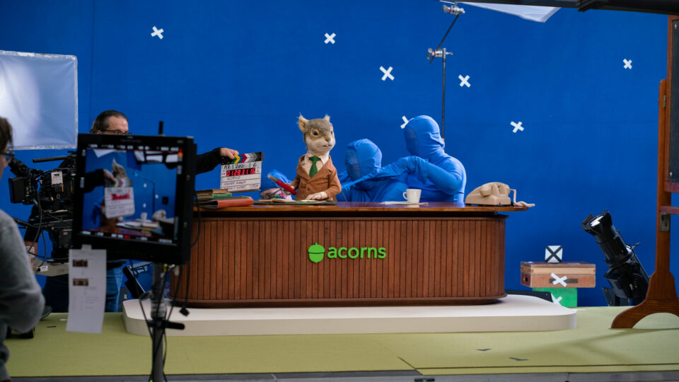 Blue screen studio shot with squirrel puppet at desk, crew filming