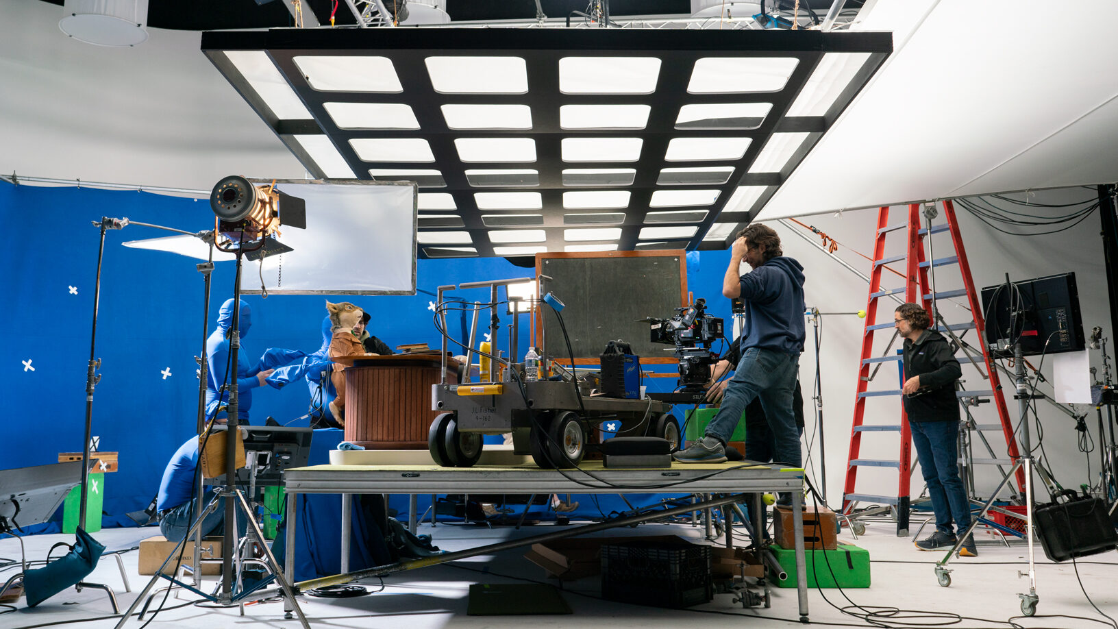 Film crew shoots scene with blue screen, lighting, and camera equipment