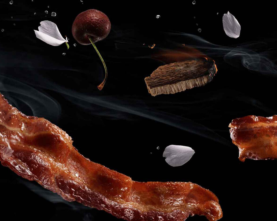 Crispy bacon, cherry, cherry blossoms, and smoke against black background
