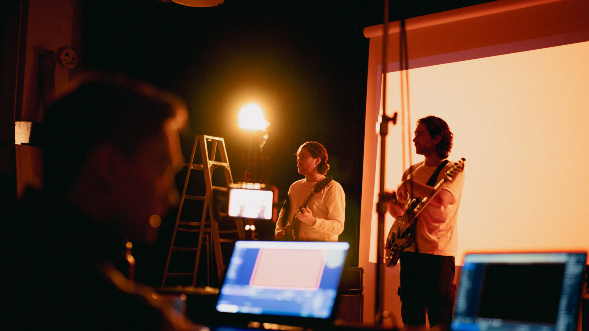 Musicians perform on stage while a technician monitors footage on laptops.