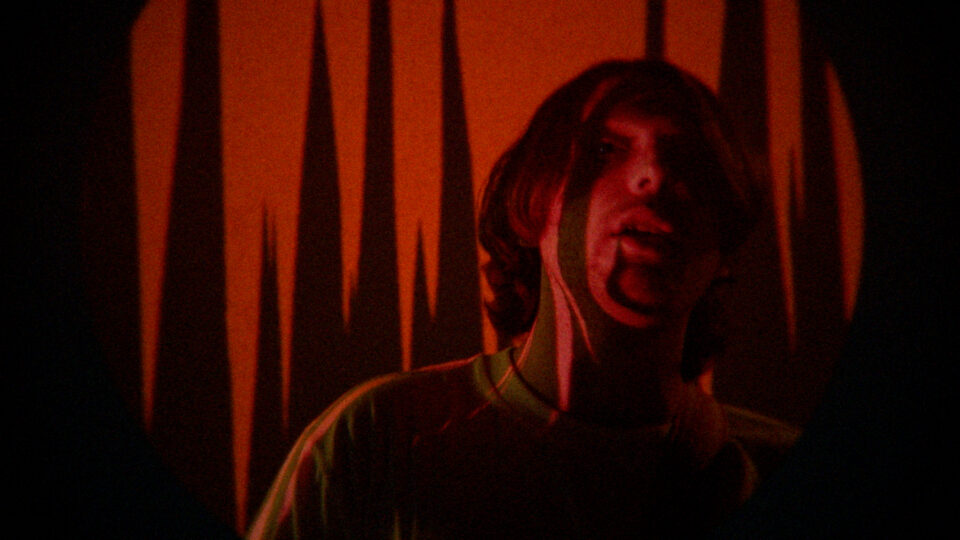 Person in dim red light with jagged shadow patterns behind them