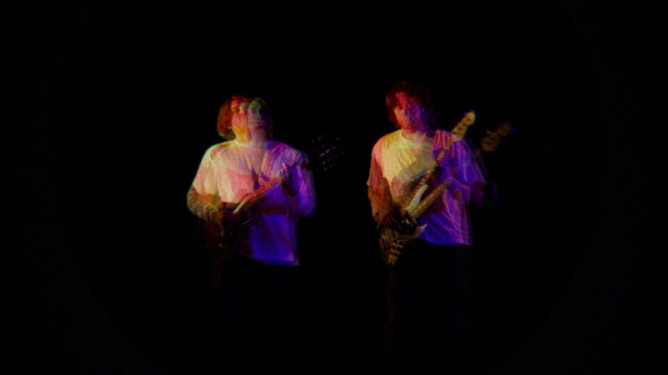 Two musicians playing guitars under colorful stage lights in darkness