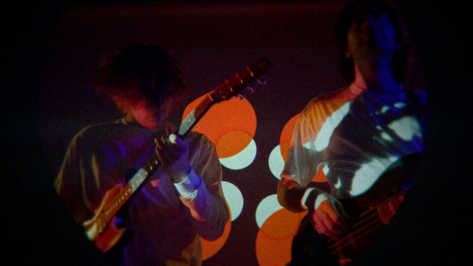 Two musicians playing guitars under colorful stage lights