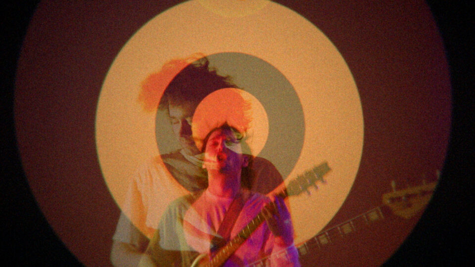 Musicians playing guitars under warm, circular stage lighting.