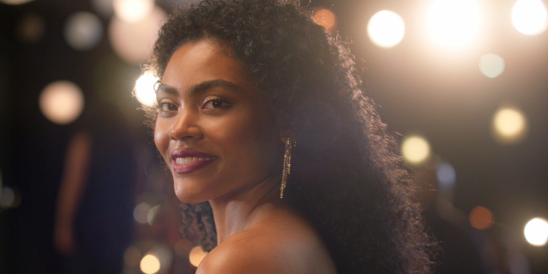 Woman with curly hair smiles at camera under bright lights